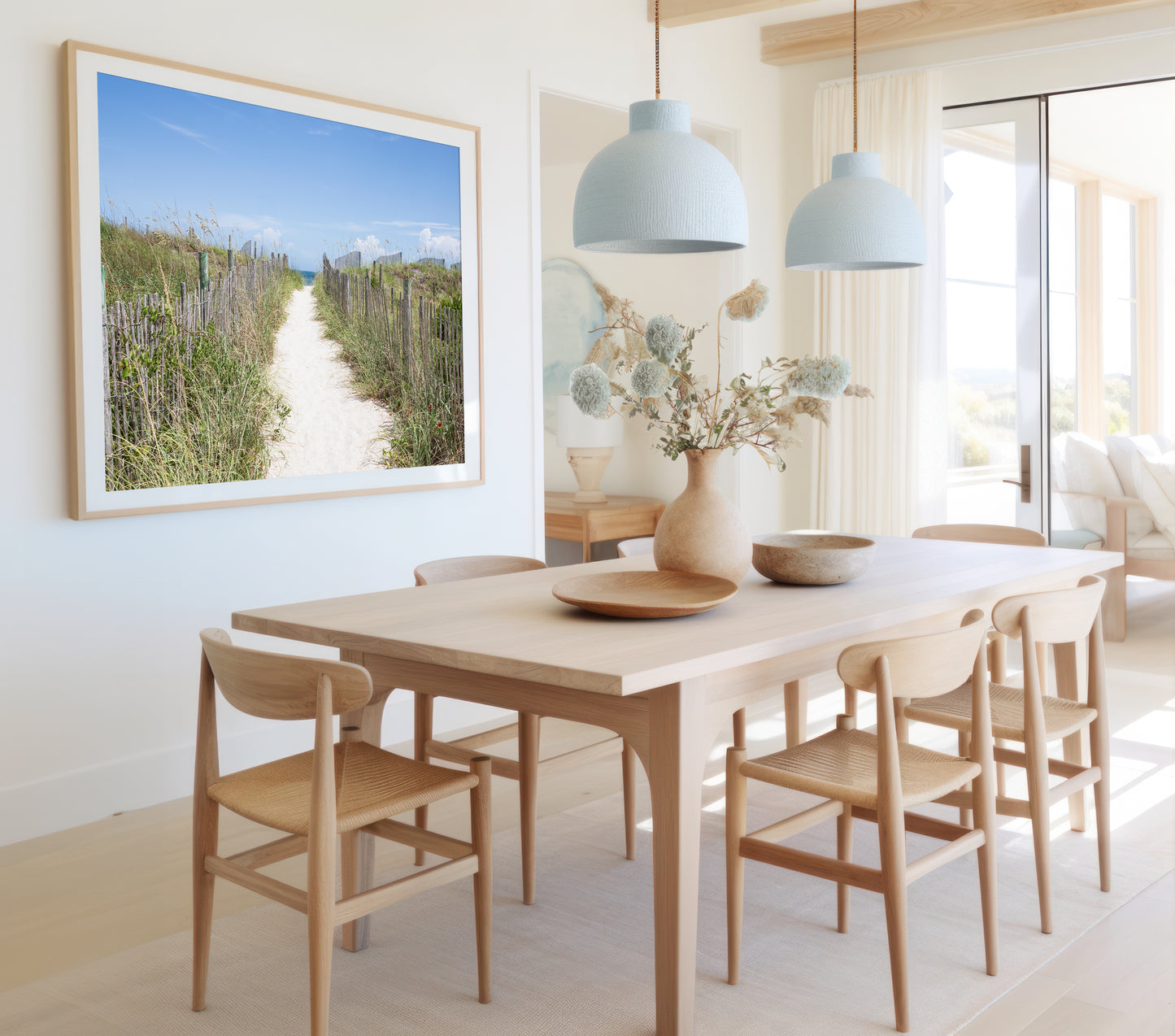Dining room with wooden table and chairs, framed picture of a beach scene, and light blue pendant lights.