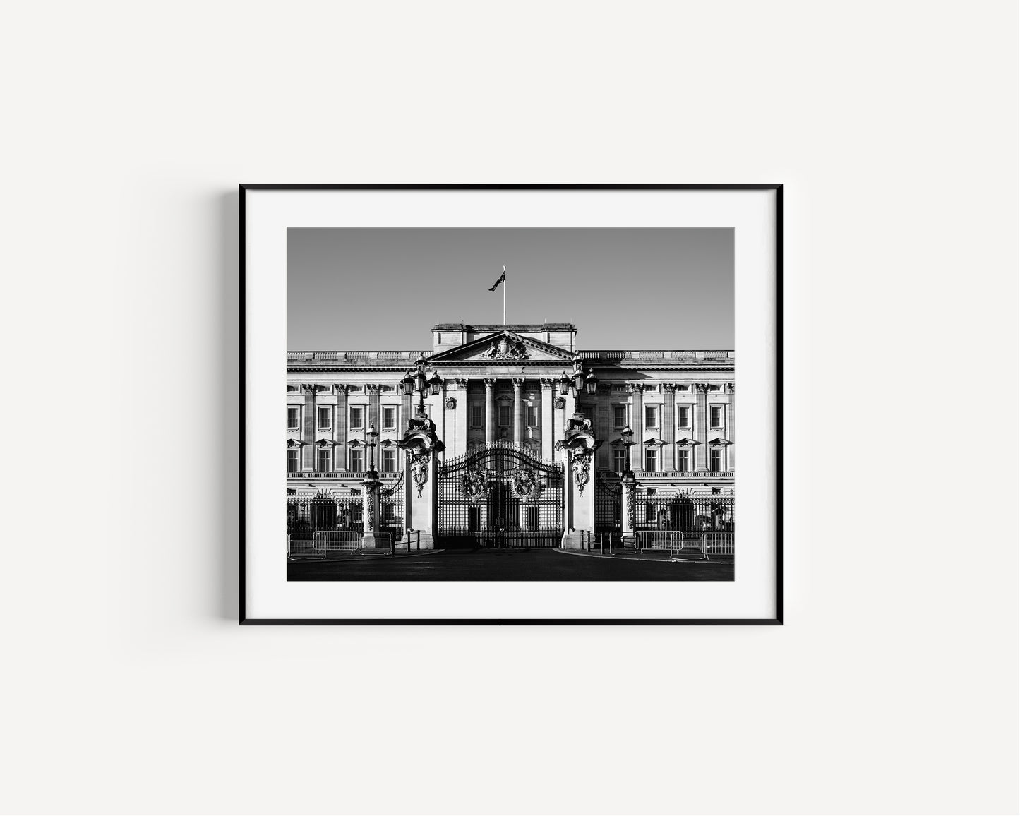 Black and white photograph of Buckingham Palace with decorative gates and clear sky, captured in London.
