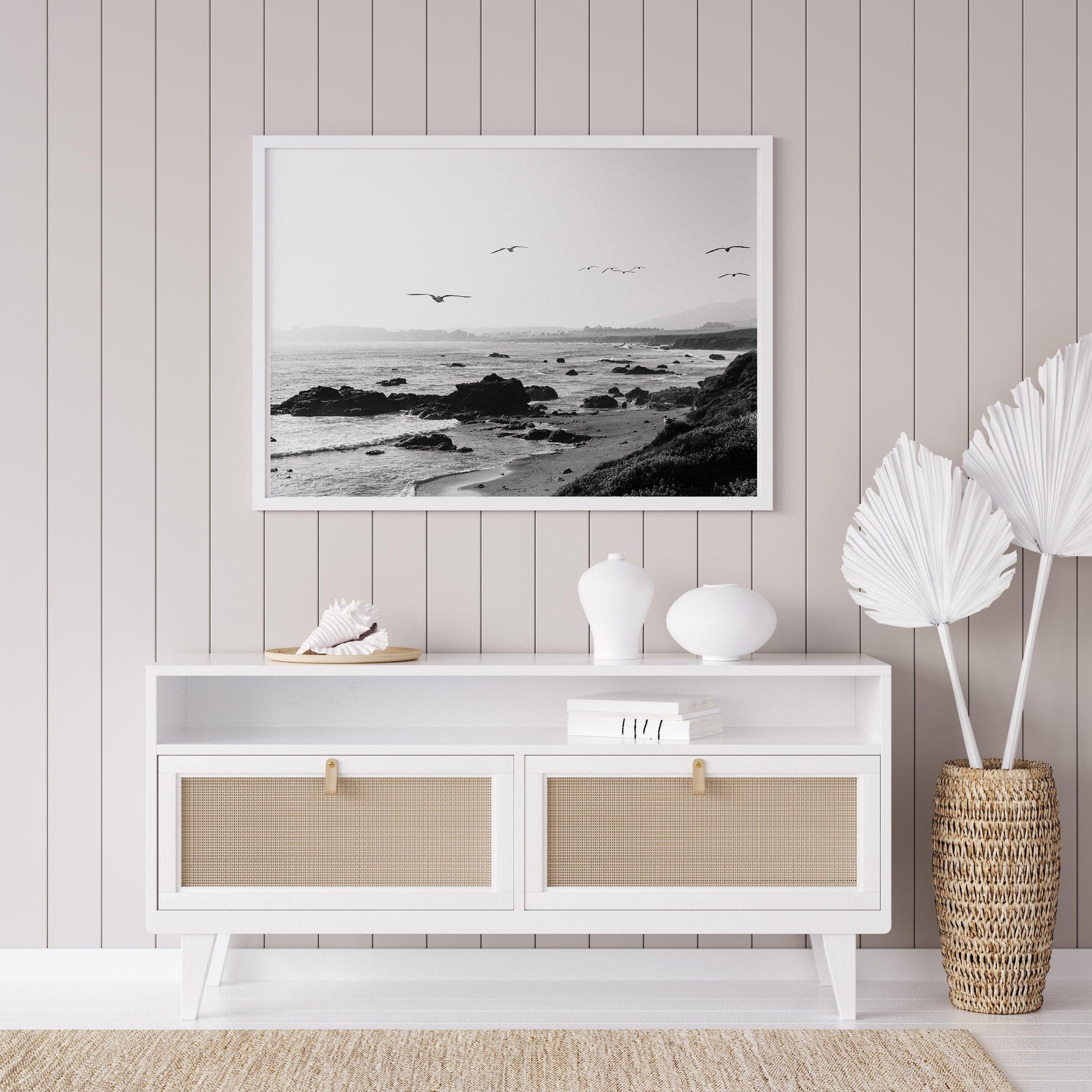 Black and white photo of birds flying over California coast with ocean waves and rocky shoreline