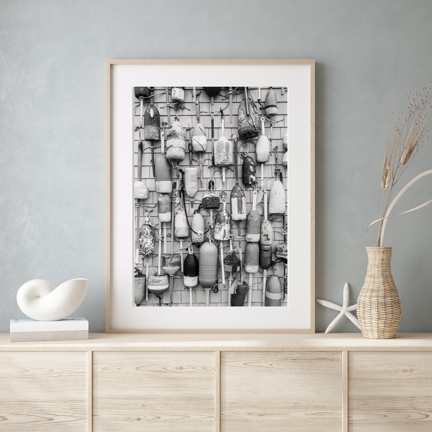 Black and white photograph of weathered fishing buoys hanging on a wood wall, captured in Cape Cod. Nautical wall art with a rustic coastal feel.