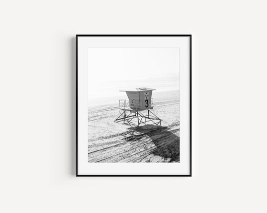 Black and white photograph of a lifeguard tower on a sandy beach.