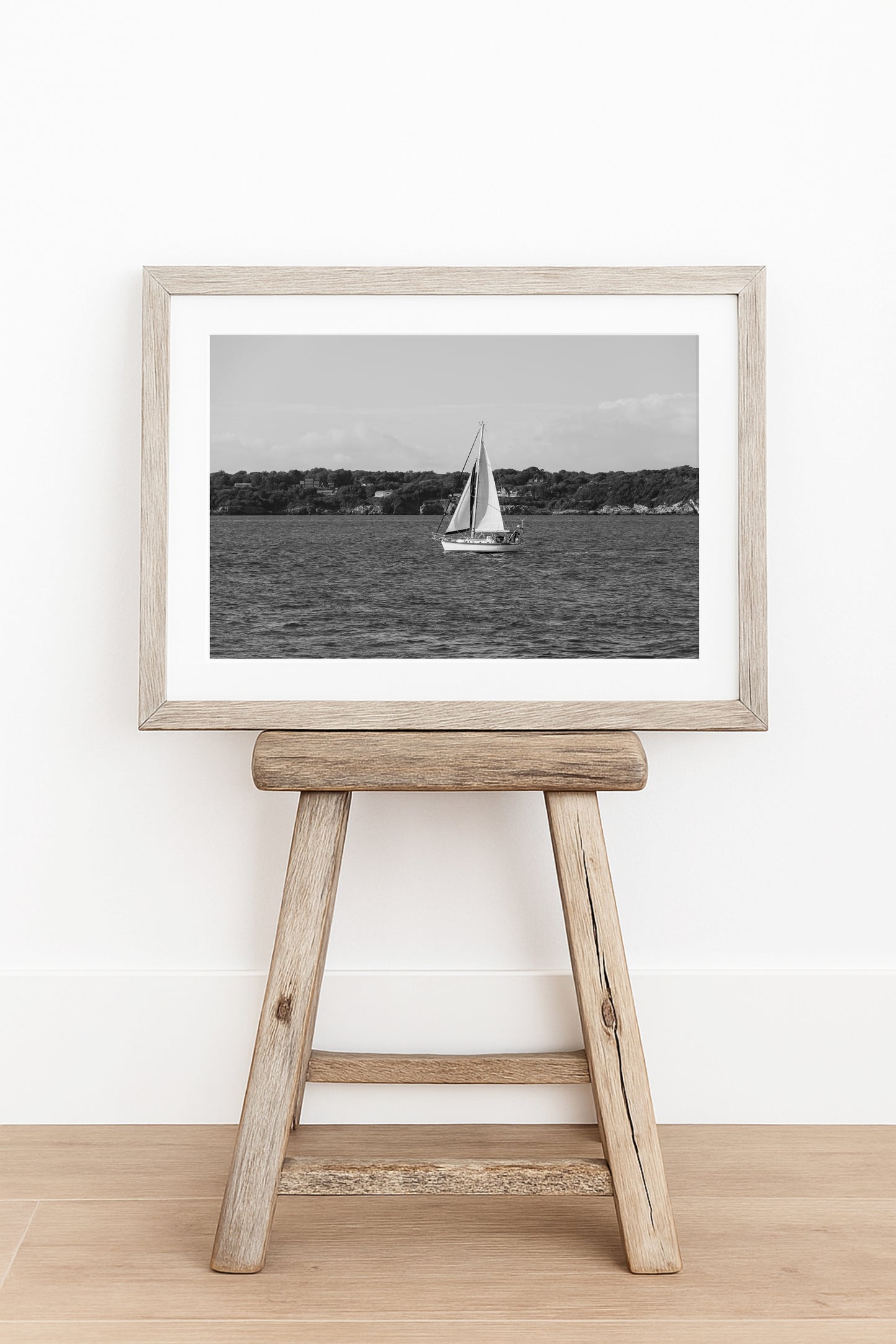 Horizontal black and white sailboat photo taken in Newport, Rhode Island, featuring a single sailboat on open water with a calm shoreline in the background. Ideal for coastal wall decor and lake house art.