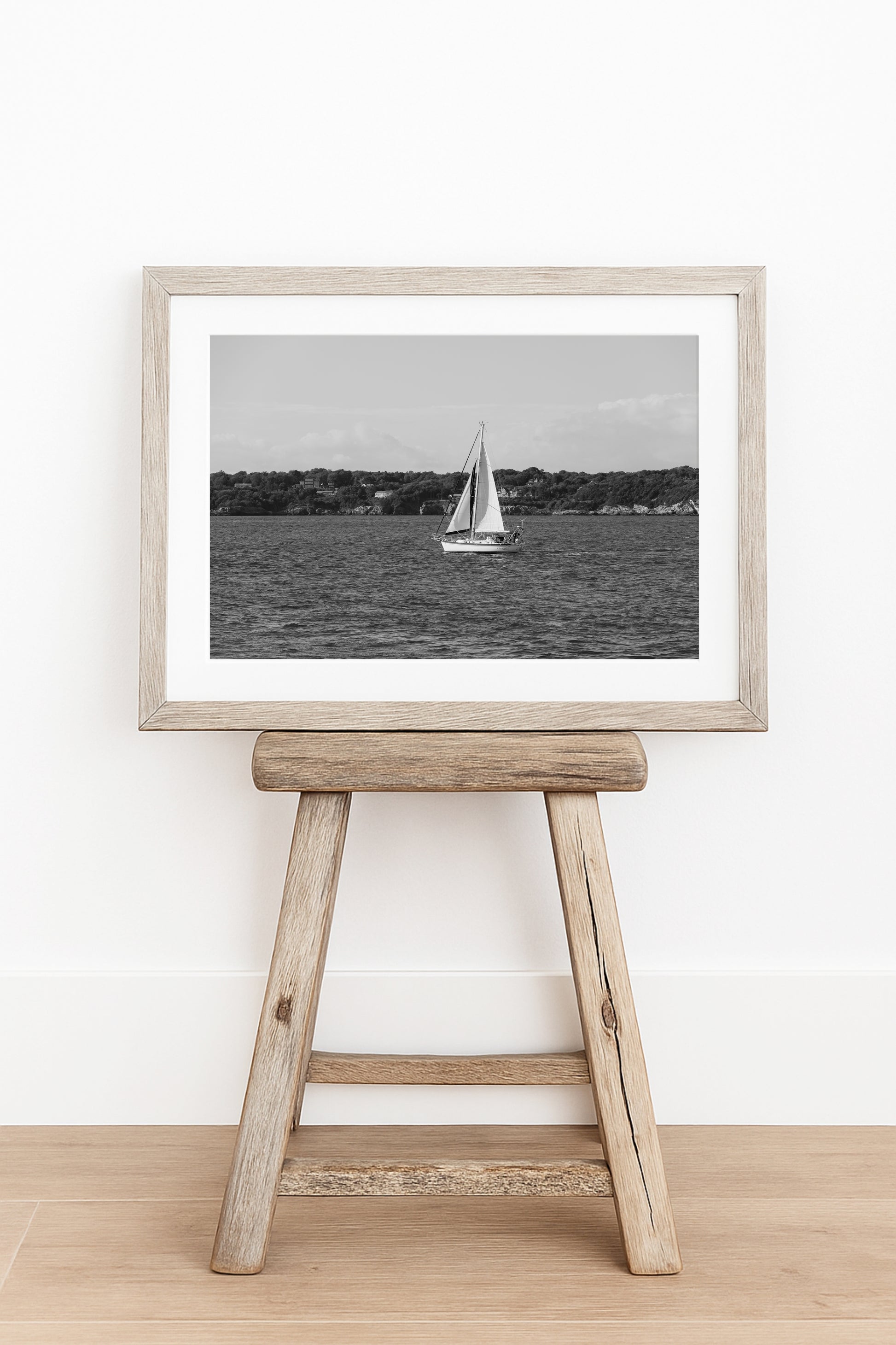 Horizontal black and white sailboat photo taken in Newport, Rhode Island, featuring a single sailboat on open water with a calm shoreline in the background. Ideal for coastal wall decor and lake house art.