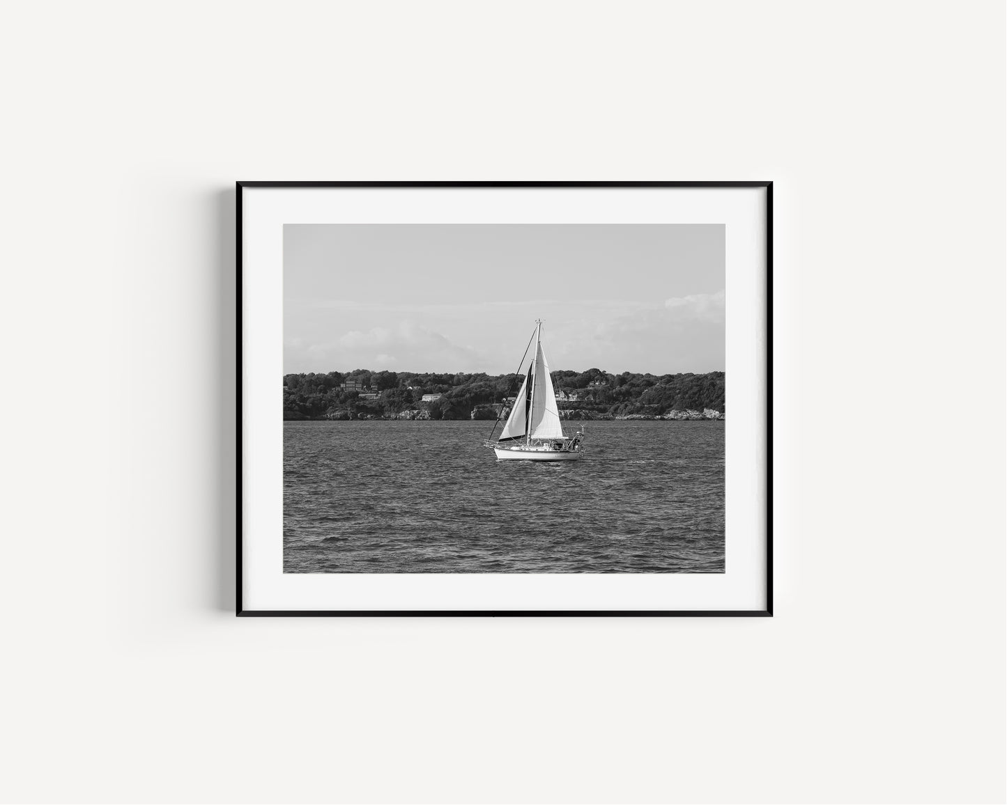 Horizontal black and white sailboat photo taken in Newport, Rhode Island, featuring a single sailboat on open water with a calm shoreline in the background. Ideal for coastal wall decor and lake house art.