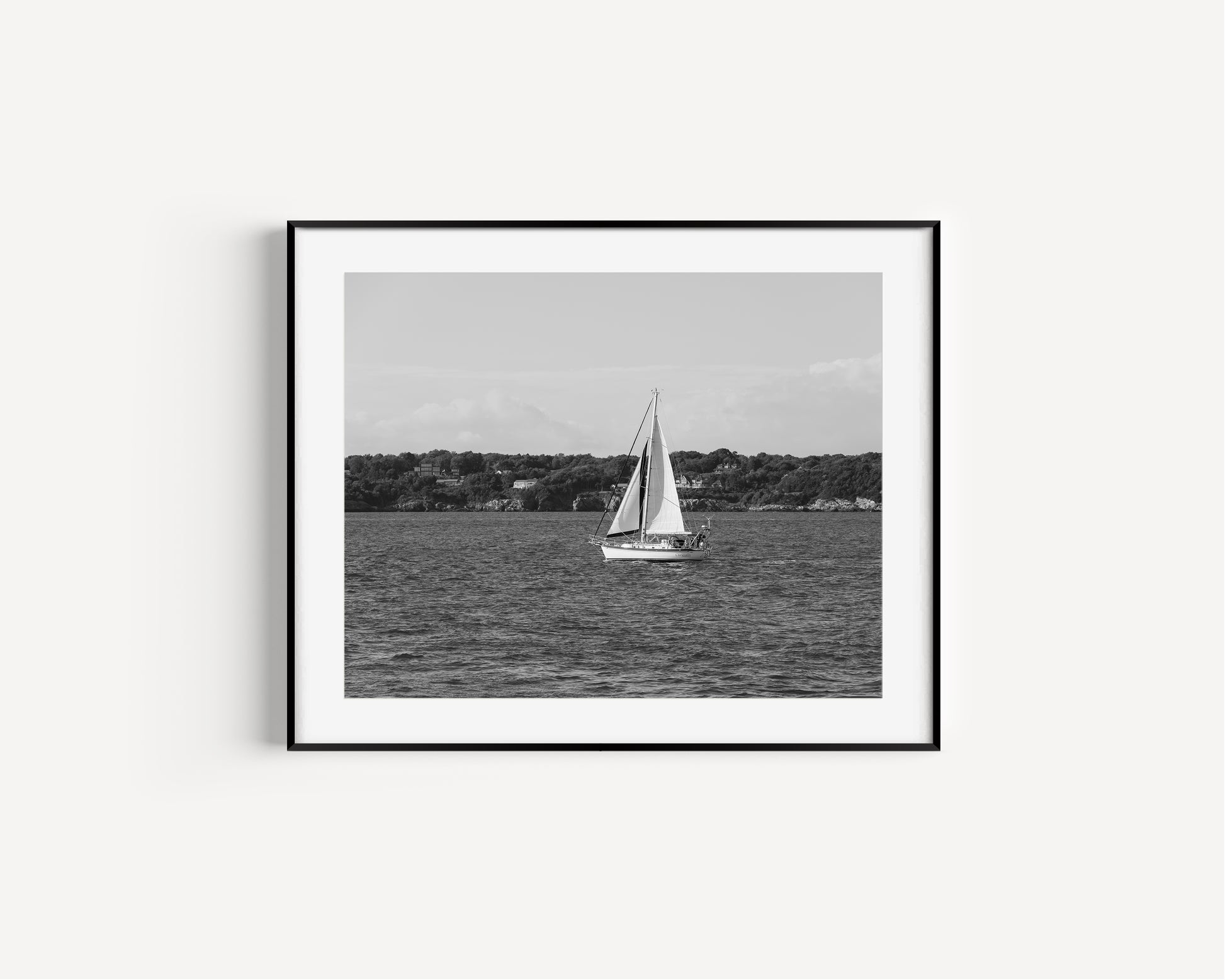 Horizontal black and white sailboat photo taken in Newport, Rhode Island, featuring a single sailboat on open water with a calm shoreline in the background. Ideal for coastal wall decor and lake house art.