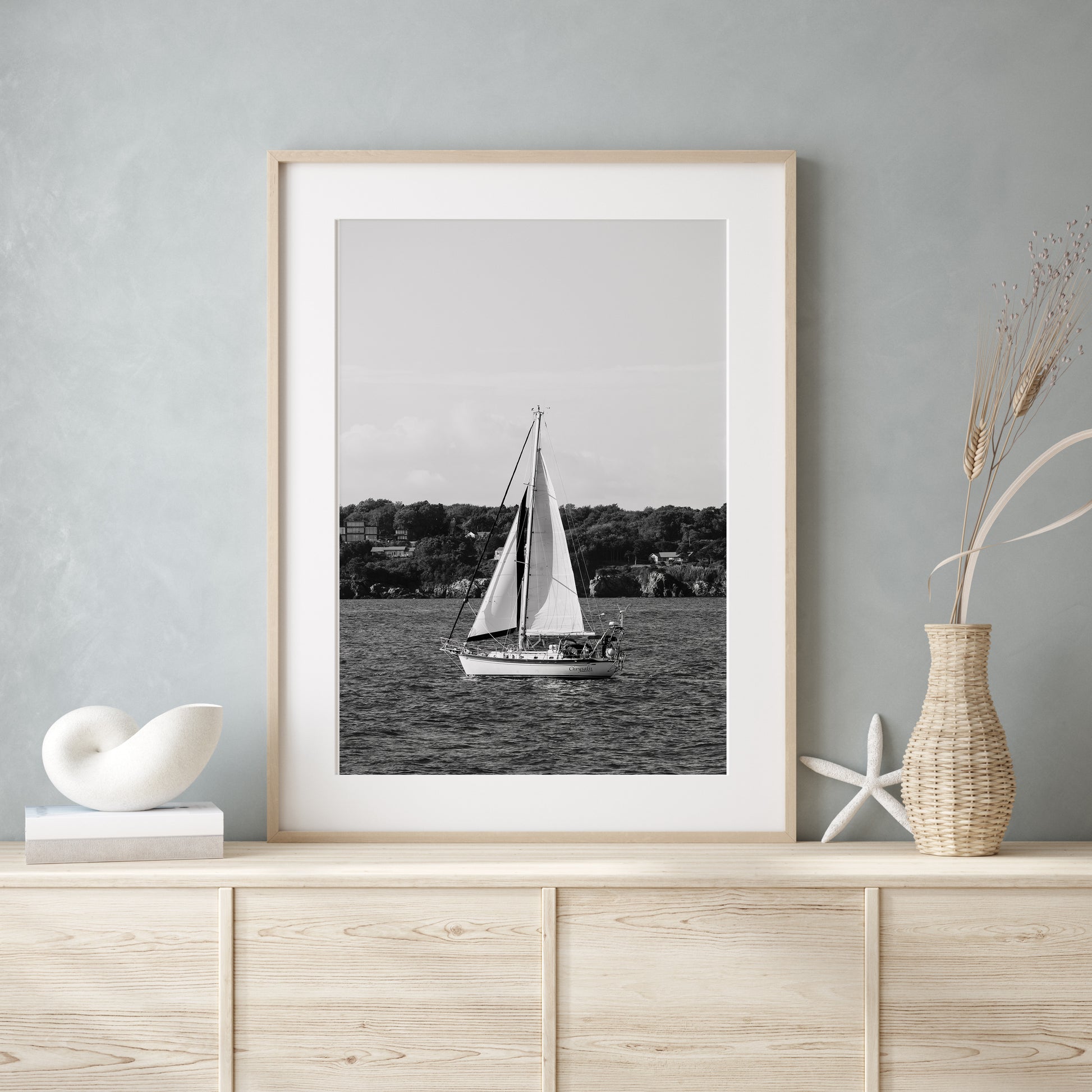 Black and white photo of a sailboat sailing in Newport, Rhode Island, with calm ocean water and soft horizon in the background. Coastal nautical wall art.