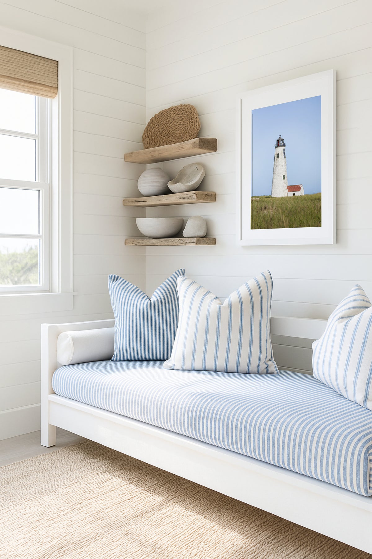 Color fine art photograph of Great Point Lighthouse at the northern tip of Nantucket Island — weathered white tower rising above green marsh grass with a small red-roofed keeper's house and pale blue sky