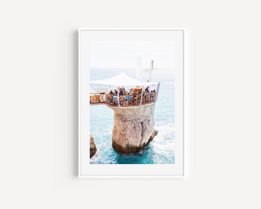 Aerial view of Le Plongeoir restaurant above the sea in Nice, France, with bright turquoise Mediterranean water and coastal cliffs.