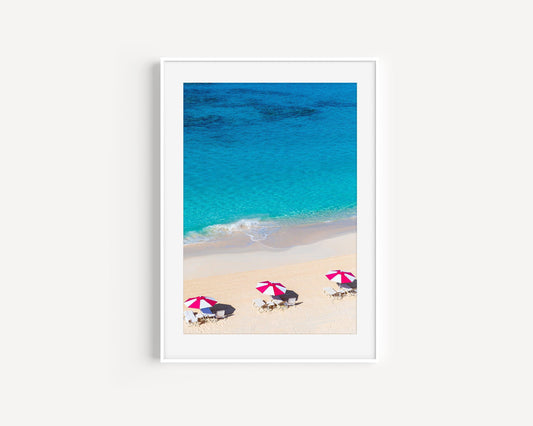 Vertical aerial view of three pink beach umbrellas on a Bermuda shoreline with turquoise ocean