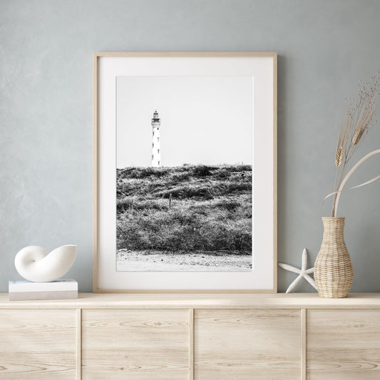 Black and white photo of the Aruba lighthouse standing tall against a bright sky, ideal for beach house decor or coastal wall art.