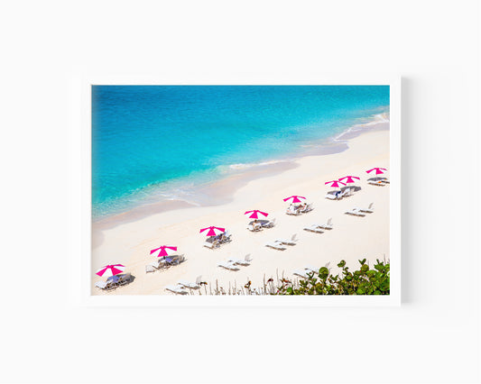Bright pink beach umbrellas on Bermuda’s sandy shore with turquoise waters in the background.