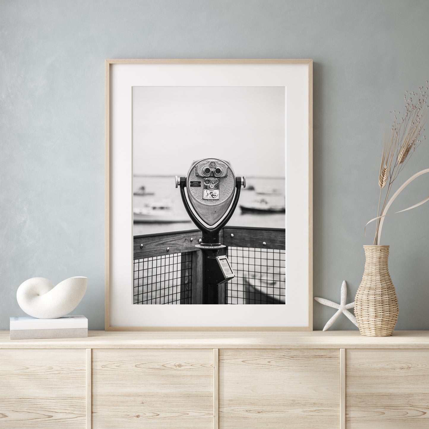 Black and white fine art photograph of a coin-operated viewfinder binoculars on Chatham Pier, Cape Cod — boats soft in the harbor background, wooden pier railing in foreground