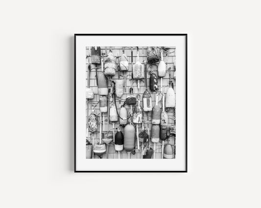 Black and white photograph of weathered fishing buoys hanging on a wood wall, captured in Cape Cod. Nautical wall art with a rustic coastal feel.