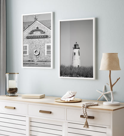 Black and white fine art photograph of Great Point Lighthouse and keeper's house on Nantucket Island — weathered white tower above dark dune grass against a flat grey sky, remote coastal wall art
