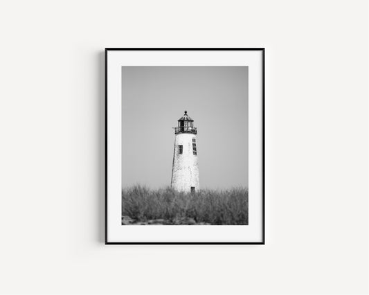 Black and white fine art photograph of Great Point Lighthouse and keeper's house on Nantucket Island — weathered white tower above dark dune grass against a flat grey sky, remote coastal wall art