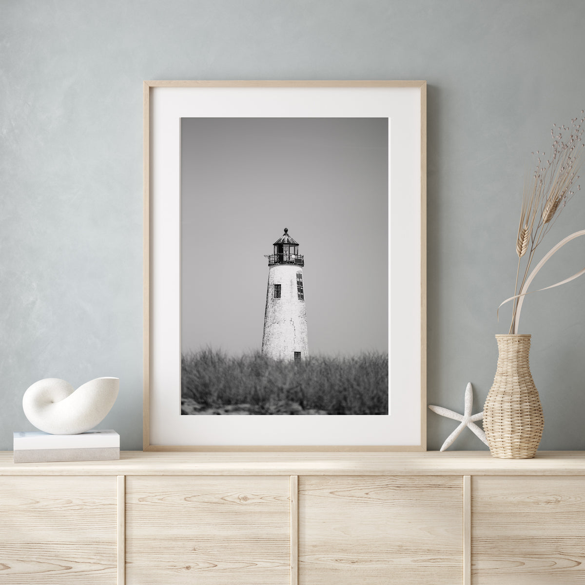 Black and white fine art photograph of Great Point Lighthouse and keeper's house on Nantucket Island — weathered white tower above dark dune grass against a flat grey sky, remote coastal wall art