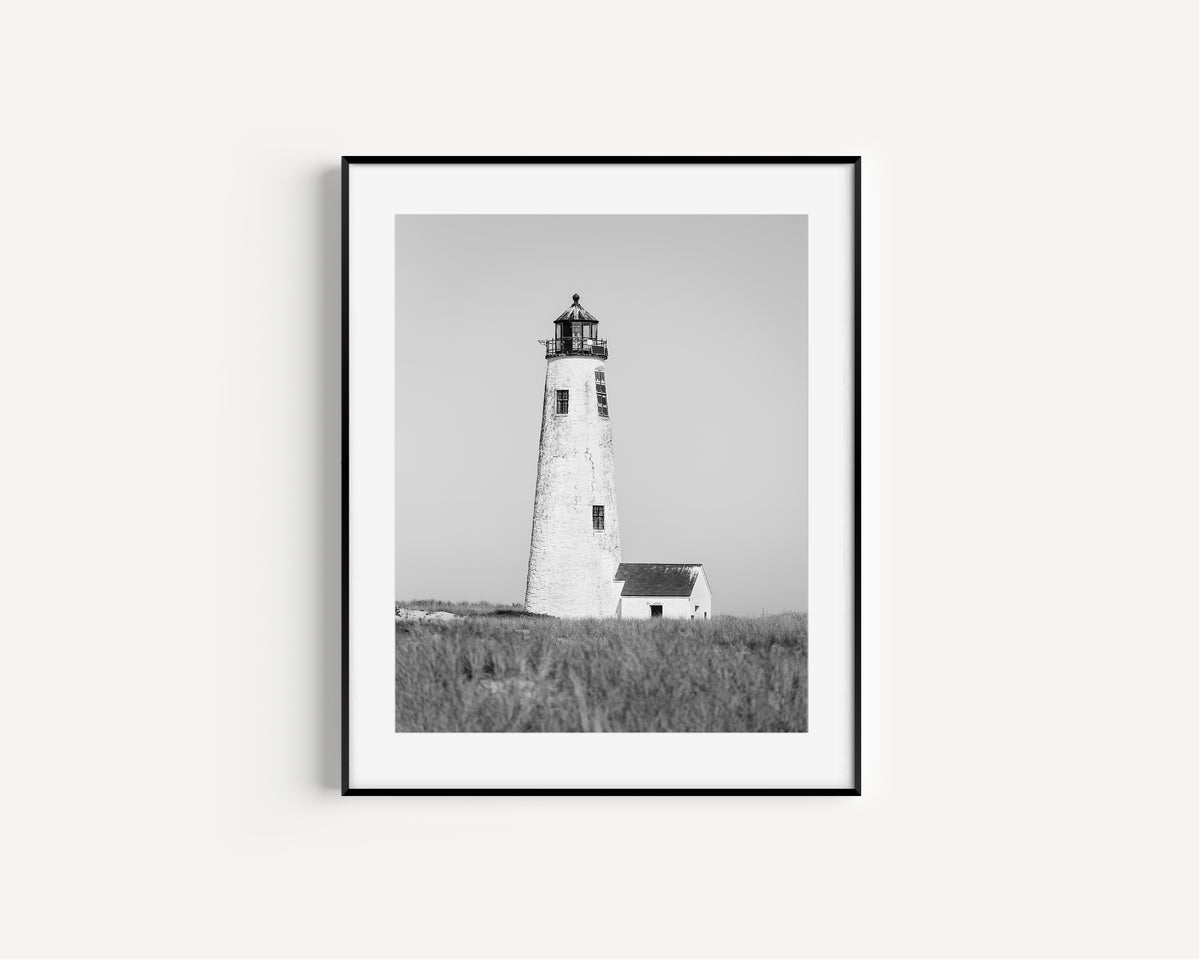 Black and white fine art photograph of Great Point Lighthouse on Nantucket Island — weathered white tower rising above dark dune grass against a flat grey sky, minimalist coastal wall art