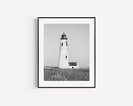 Black and white fine art photograph of Great Point Lighthouse on Nantucket Island — weathered white tower rising above dark dune grass against a flat grey sky, minimalist coastal wall art