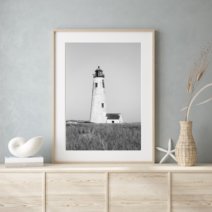 Black and white fine art photograph of Great Point Lighthouse on Nantucket Island — weathered white tower rising above dark dune grass against a flat grey sky, minimalist coastal wall art