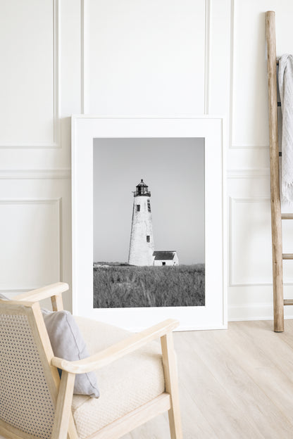 Black and white fine art photograph of Great Point Lighthouse on Nantucket Island — weathered white tower rising above dark dune grass against a flat grey sky, minimalist coastal wall art
