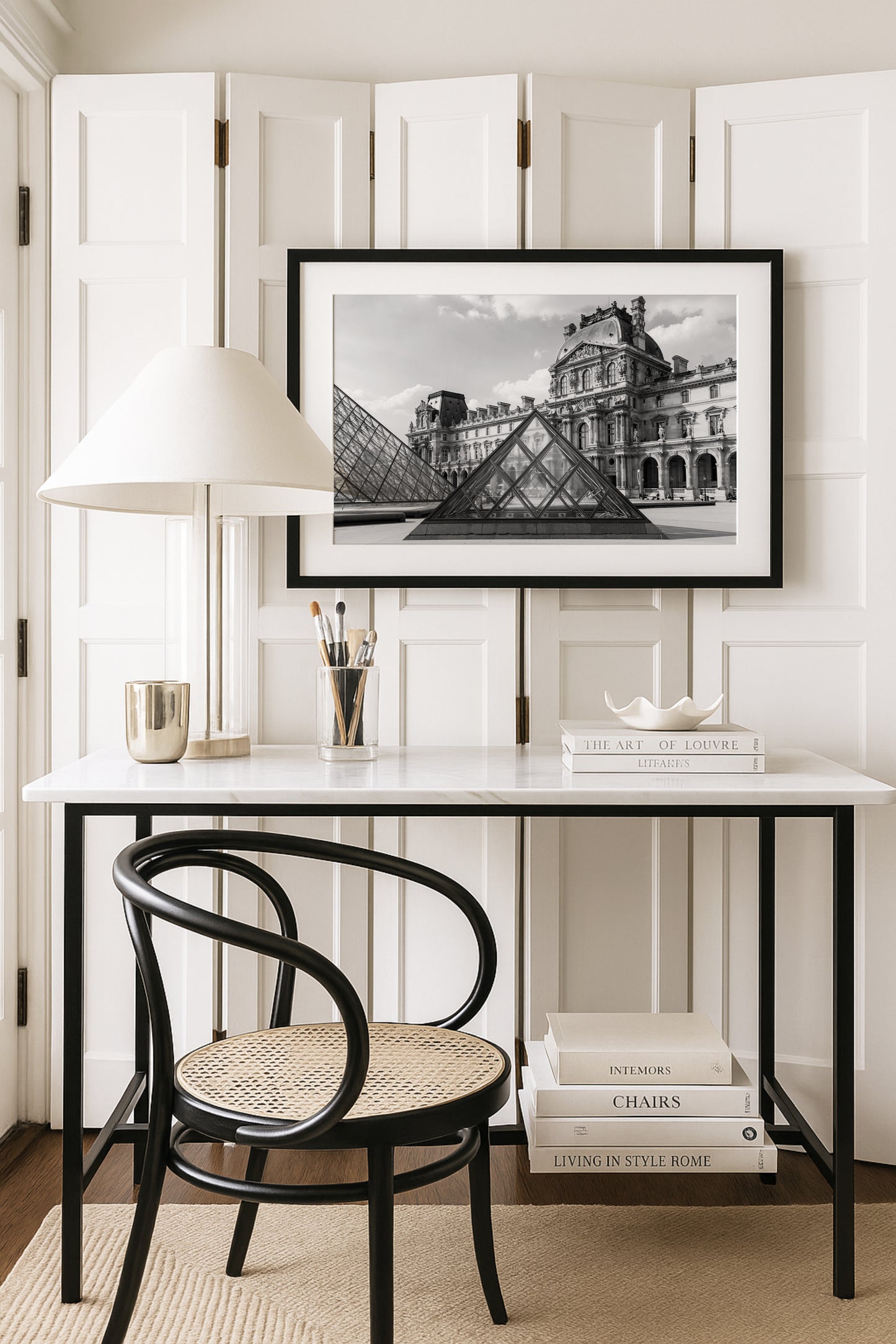 Black and white photograph of the Louvre Museum in Paris with its glass pyramids in the courtyard under a partly cloudy sky.
