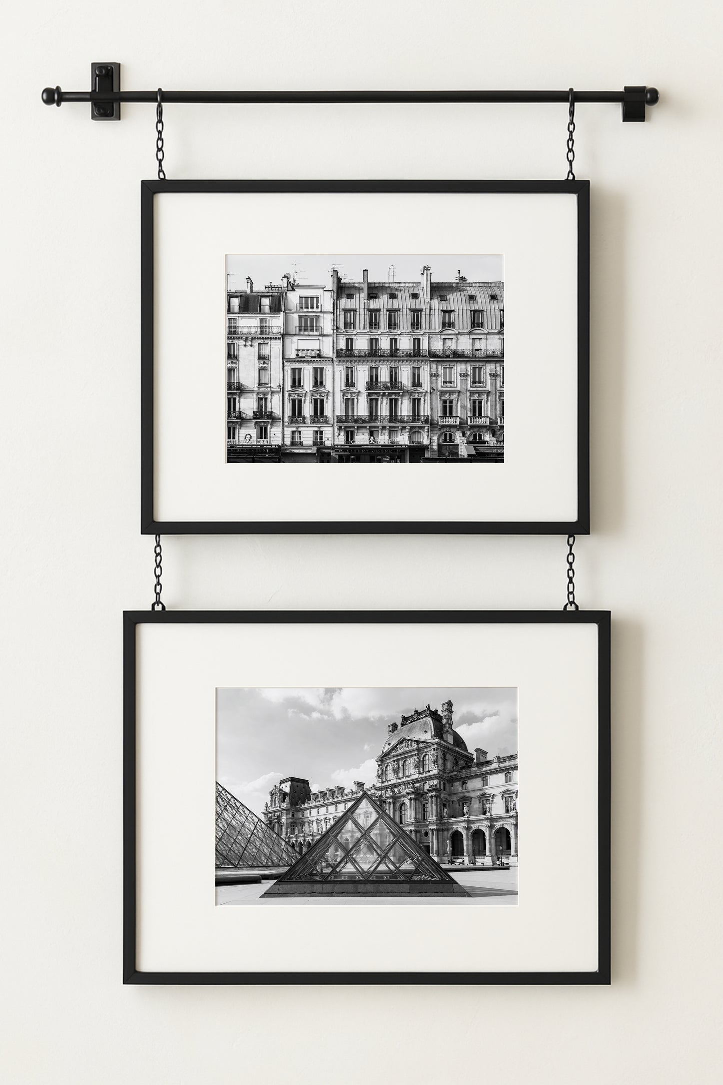Black and white photograph of the Louvre Museum in Paris with its glass pyramids in the courtyard under a partly cloudy sky.