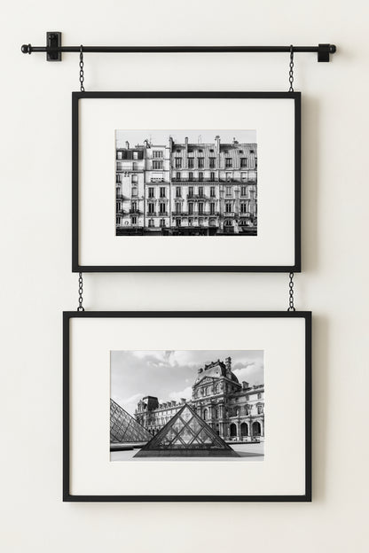 Black and white photograph of the Louvre Museum in Paris with its glass pyramids in the courtyard under a partly cloudy sky.