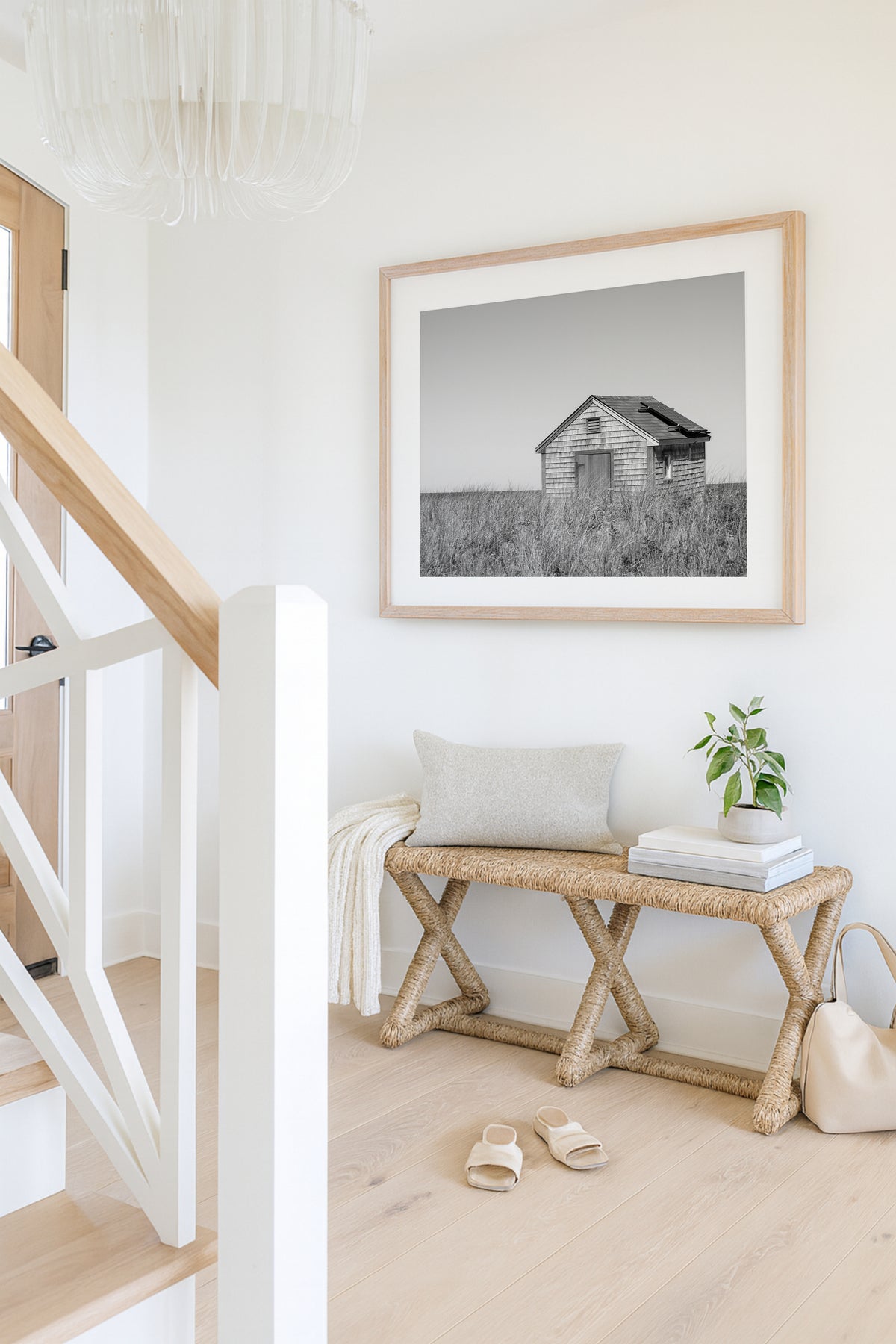 Black and white fine art photograph of a weathered cedar shingle beach cottage alone in wild dune grass on Nantucket Island — flat grey sky above, ocean just visible on the horizon