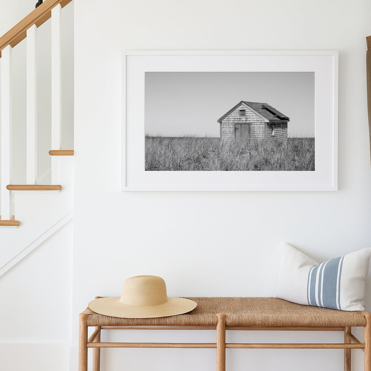 Black and white fine art photograph of a weathered cedar shingle beach cottage alone in wild dune grass on Nantucket Island — flat grey sky above, ocean just visible on the horizon