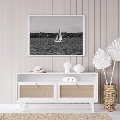 Horizontal black and white sailboat photo taken in Newport, Rhode Island, featuring a single sailboat on open water with a calm shoreline in the background. Ideal for coastal wall decor and lake house art.