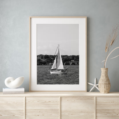 Black and white photo of a sailboat sailing in Newport, Rhode Island, with calm ocean water and soft horizon in the background. Coastal nautical wall art.