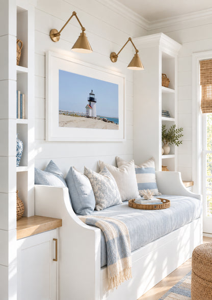 Color fine art photograph of Brant Point Lighthouse on Nantucket shot from the beach, white tower with red-roofed keeper's entrance, white fence boardwalk on the left and harbor water on both sides