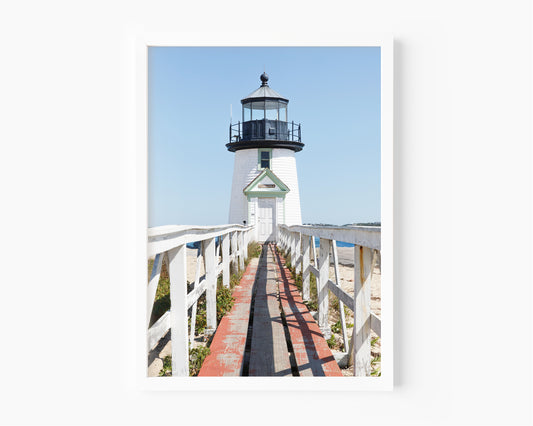 Vertical photograph of Brant Point Lighthouse in Nantucket, viewed straight down the weathered boardwalk with a bright blue sky and soft coastal light.