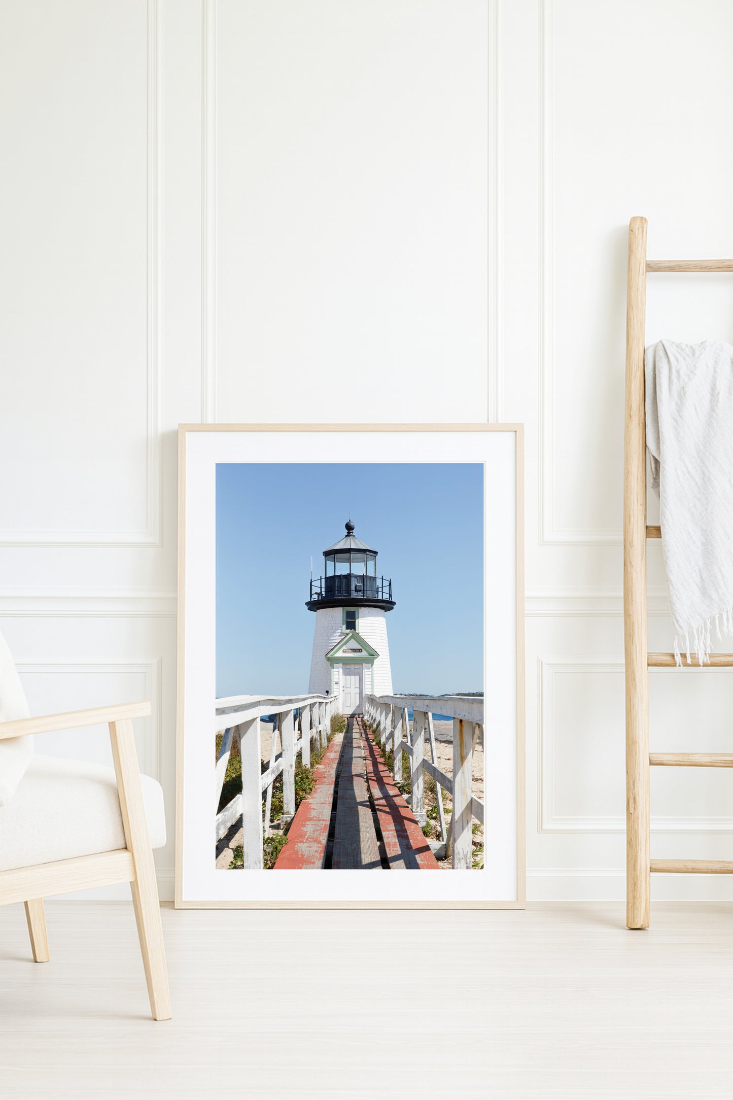 Vertical photograph of Brant Point Lighthouse in Nantucket, viewed straight down the weathered boardwalk with a bright blue sky and soft coastal light.