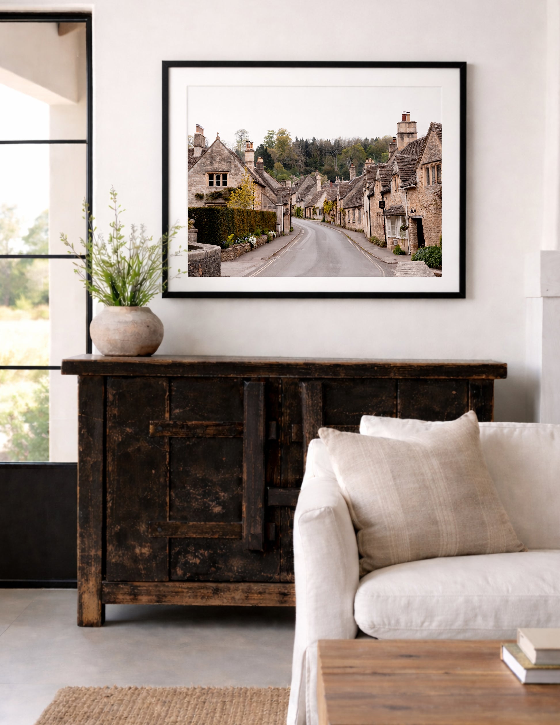 Color fine art photograph of Castle Combe village in the Cotswolds, England — empty road winding through honey-stone cottages with woodland rising behind the rooftops