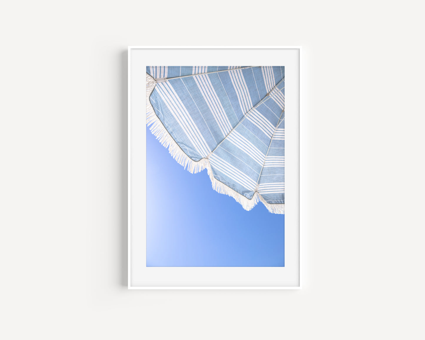 Vertical photo of striped blue beach umbrella with fringe and bright blue sky – coastal summer wall art