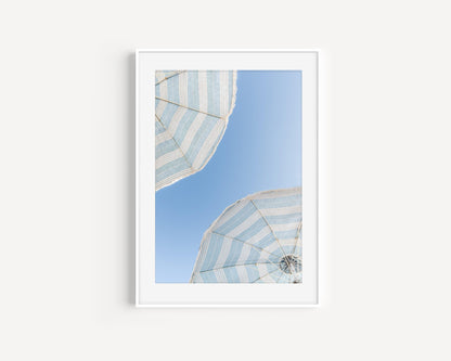 Two blue and white striped beach umbrellas set against a clear blue sky.