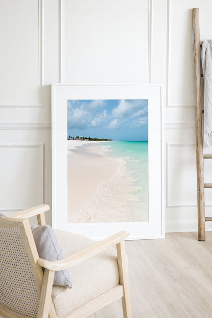 Color fine art photograph of Eagle Beach in Aruba — powder white sand, turquoise Caribbean water with a gentle wave at the shoreline, and palapa huts visible in the distance