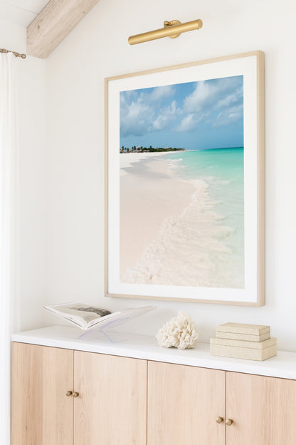 Color fine art photograph of Eagle Beach in Aruba — powder white sand, turquoise Caribbean water with a gentle wave at the shoreline, and palapa huts visible in the distance
