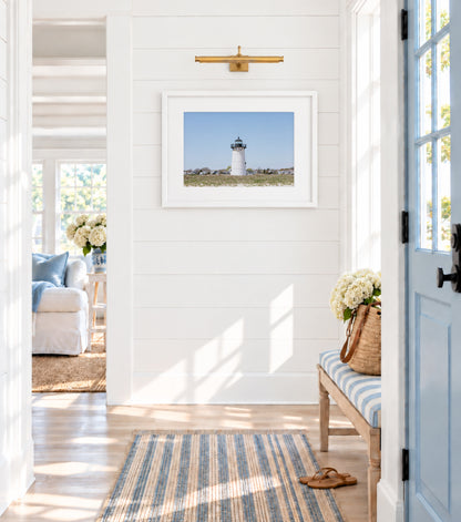 Color fine art photograph of the Edgartown Lighthouse on Martha's Vineyard, white tower centered against a pale blue sky with beach grass in the foreground and Edgartown village behind it
