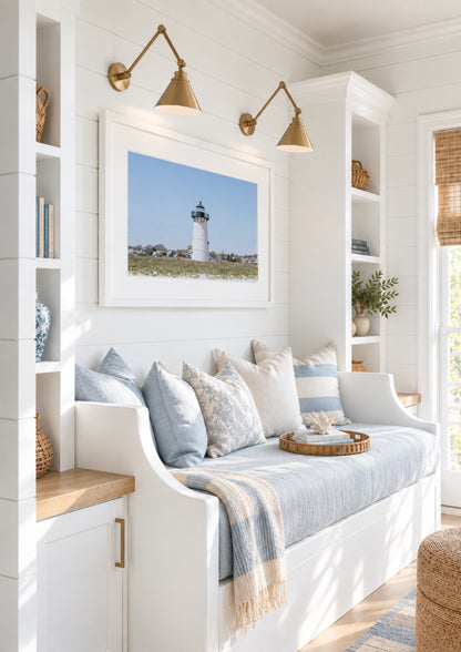 Color fine art photograph of the Edgartown Lighthouse on Martha's Vineyard, white tower centered against a pale blue sky with beach grass in the foreground and Edgartown village behind it