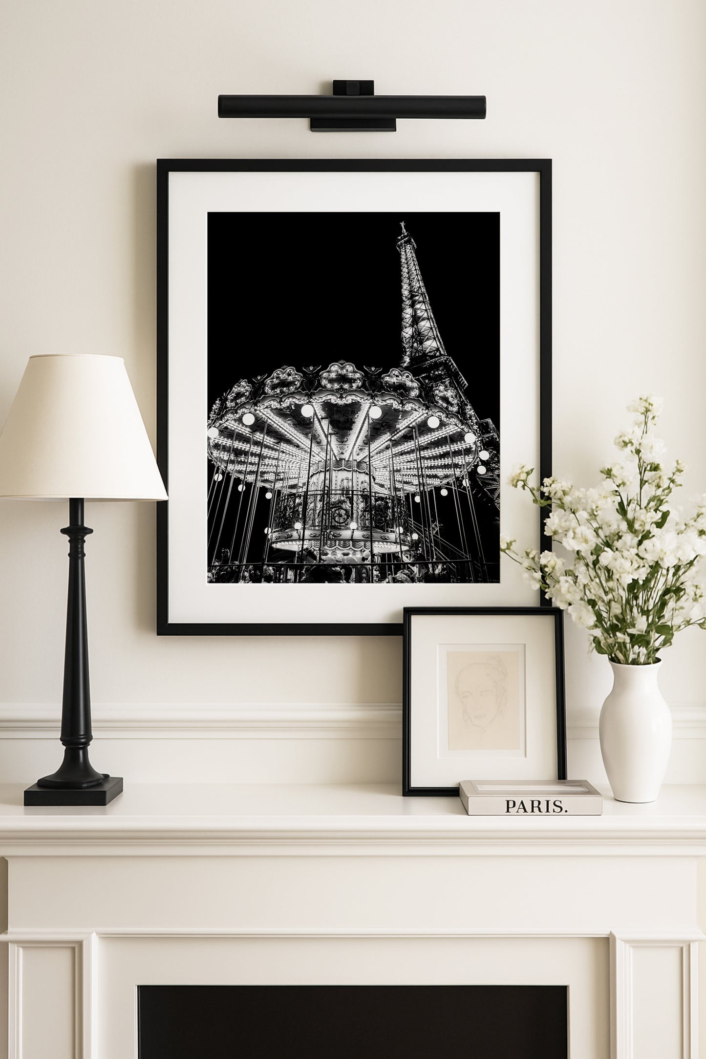 Black and white photo of the Eiffel Tower at night with an illuminated Paris carousel in the foreground.