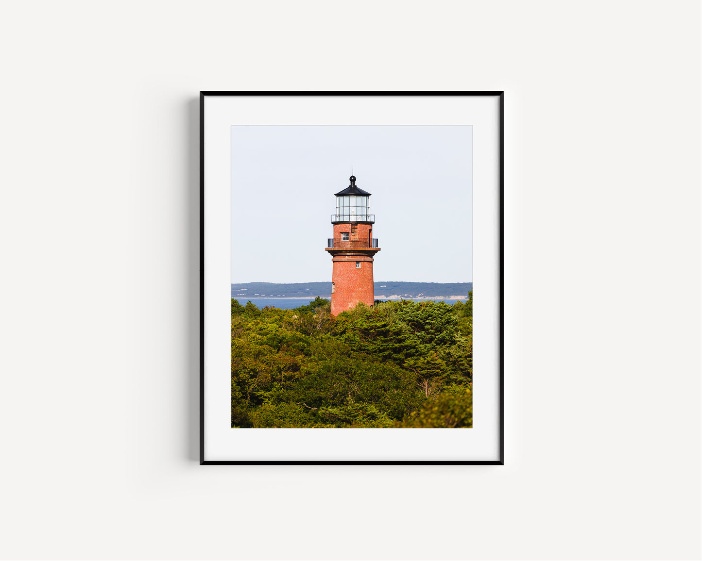 Lighthouse photo showing the red brick Gay Head Lighthouse above lush greenery in Aquinnah, Mass, with the Martha’s Vineyard coastline in the background.