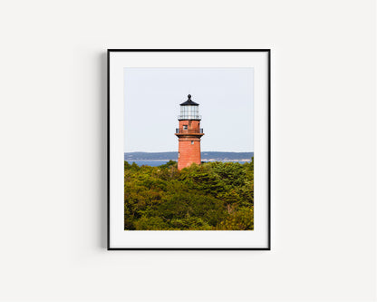 Lighthouse photo showing the red brick Gay Head Lighthouse above lush greenery in Aquinnah, Mass, with the Martha’s Vineyard coastline in the background.