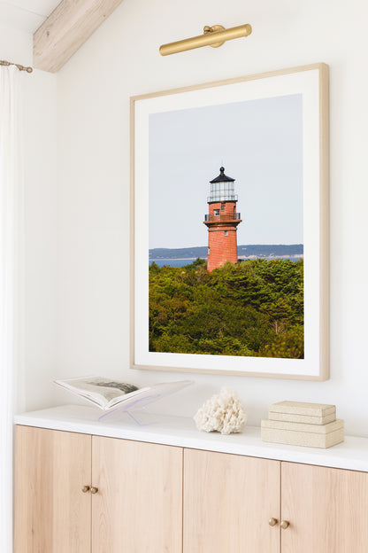 Lighthouse photo showing the red brick Gay Head Lighthouse above lush greenery in Aquinnah, Mass, with the Martha’s Vineyard coastline in the background.