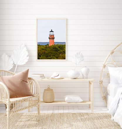 Lighthouse photo showing the red brick Gay Head Lighthouse above lush greenery in Aquinnah, Mass, with the Martha’s Vineyard coastline in the background.