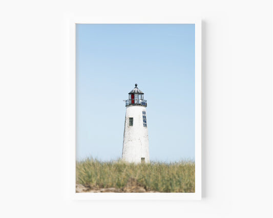 Color fine art photograph of Great Point Lighthouse on Nantucket Island — weathered white tower centered against a wide pale blue sky with dune grass at the base, minimalist coastal wall art