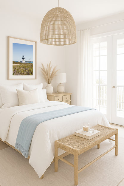 Brant Point Lighthouse stands at the edge of Nantucket Harbor, framed by dune grass with sailboats and a schooner in the background under a clear blue sky.