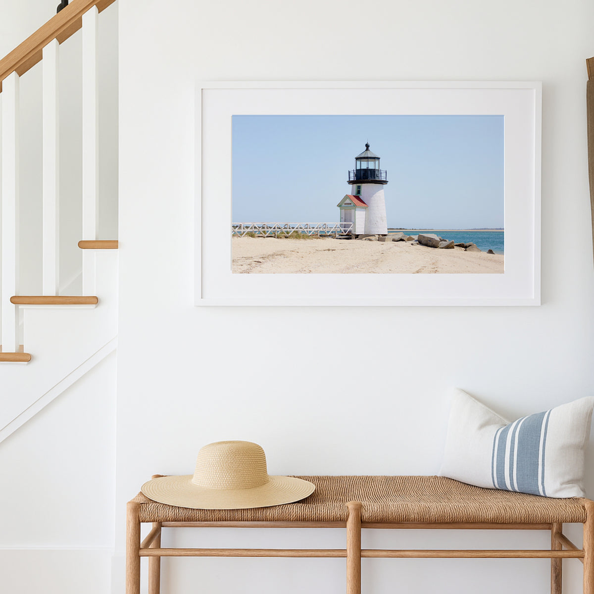 Color fine art photograph of Brant Point Lighthouse on Nantucket shot from the beach, white tower with red-roofed keeper's entrance, white fence boardwalk on the left and harbor water on both sides