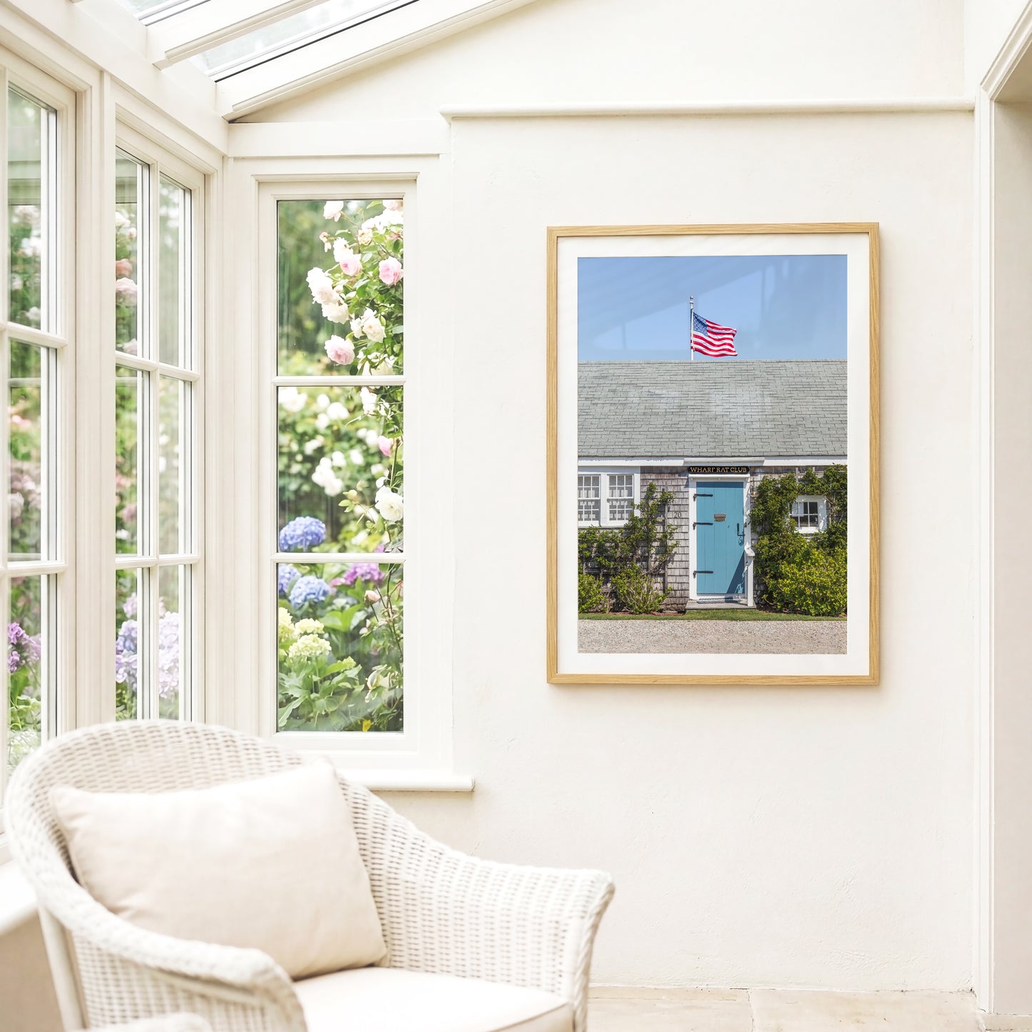 Color fine art photograph of the Wharf Rat Club on Nantucket — weathered grey shingle cottage with a powder blue door, climbing vines, and an American flag flying above the roofline against a blue summer sky